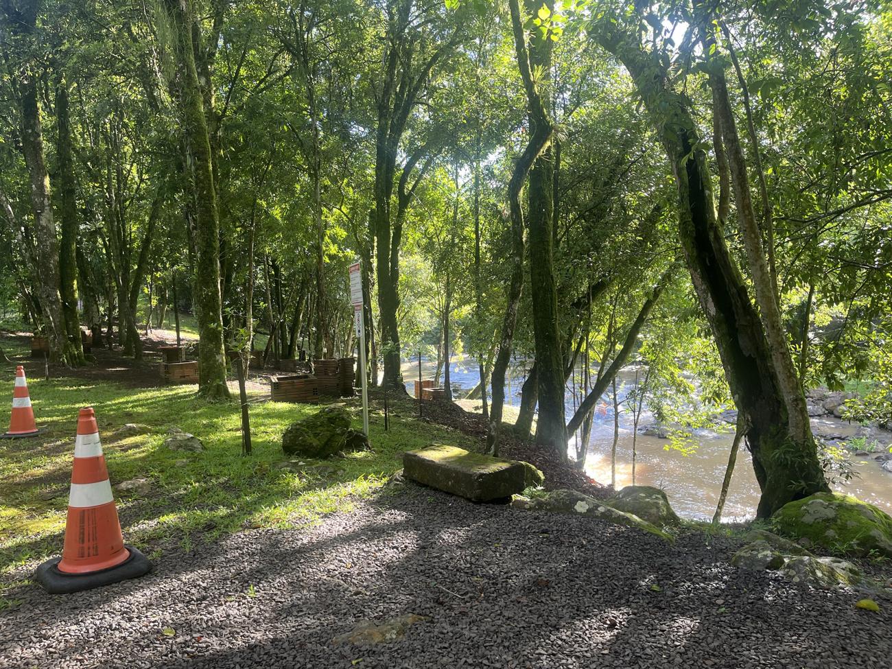Caminho de brita com churrasqueiras entre as árvores, junto ao rio