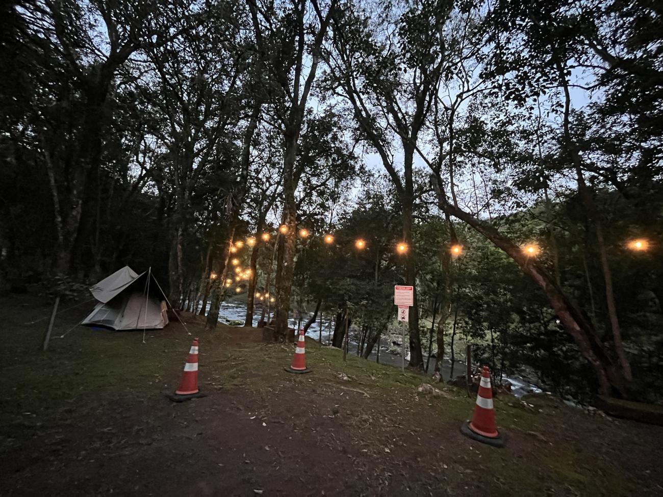 Barraca montada ao entardecer sob varais de luz, com o rio ao fundo
